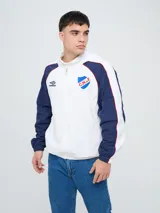 Campera deportiva Umbro del Club Nacional de Football, modelo Venti, para hombre. Diseño en color blanco con mangas azules y detalles de líneas rojas. Cuenta con capucha con cordón ajustable, cierre frontal y bolsillos. Presenta el logo de Umbro y el escudo del club bordados en el pecho.