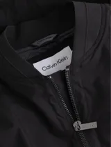 Campera bomber Calvin Klein negra, de corte regular, con cuello, puños y bajo de punto de canalé. Cierre frontal con cremallera, bolsillo con cremallera en la manga izquierda y bolsillos de hendidura en la cintura. Forro de malla e insignia con el logo de goma de Calvin Klein en la manga.