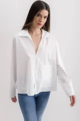 Camisa blanca de algodón, de corte holgado, con cuello clásico, mangas largas con puños anchos y un bolsillo de parche en el lateral.