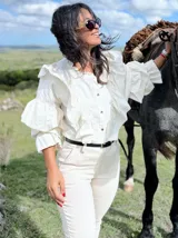 Camisa de color natural con diseño de volados en el frente y en las mangas. Presenta cuello redondo, cierre frontal con botones y mangas tres cuartos con volumen.