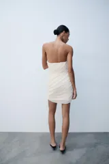 Vestido mini palabra de honor color crudo, con diseño drapeado en diagonal y cierre lateral con cremallera oculta.