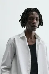 Camisa blanca de corte slim fit, confeccionada en tejido de algodón. Presenta cuello italiano, manga larga con puño abotonado y cierre frontal de botonadura.