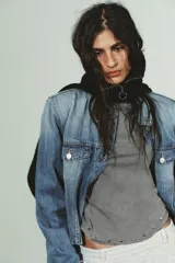 Camiseta de manga larga color gris con efecto lavado, cuello redondo y bajo redondeado. Presenta aplicaciones de tachas metálicas alrededor del escote y en el bajo.