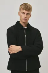 Campera negra de nylon levemente acolchada, con cuello y cierre frontal plateado. Presenta bolsillos insertados al bies y un bolsillo interior con botón a presión. Posee cordón elástico ajustable en el bajo.
