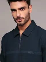 Chomba de manga corta Calvin Klein color azul marino, con cuello polo y cierre frontal parcial con cremallera. Presenta una banda horizontal en el pecho con el logo de la marca bordado.
