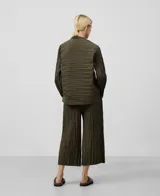 Camisa plisada color verde militar, de cuello redondo y manga larga. Tiene cierre con botones, bolsillo plastrón en el pecho y bajo redondeado.