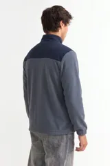 Campera de polar con cierre frontal completo, cuello alto y diseño bicolor en gris y negro. Cuenta con bolsillos laterales y puños elásticos.