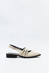 Zueco destalonado color beige con tiras finas y hebillas metálicas plateadas en el empeine. Tiene punta fina y un pequeño taco cuadrado negro.