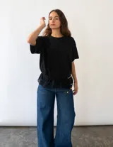 Remera de algodón color negro, de corte holgado y manga corta, con un delicado detalle de encaje en el ruedo inferior.