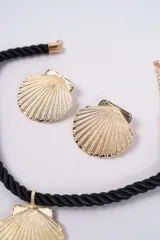 Set compuesto por un collar de cordón trenzado negro con dije central en forma de concha dorada y un par de aros a juego con diseño de concha dorada.