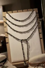 Corbatín largo de cordón negro con cuentas plateadas distribuidas a lo largo de toda la pieza. Su diseño versátil permite usarlo con múltiples vueltas alrededor del cuello o como un collar tipo lariat ajustable.