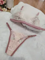 Conjunto de lencería compuesto por bralette y tanga regulable, confeccionado en encaje color champagne con detalles florales bordados en hilo rosado y terminaciones en cinta color rosa viejo.