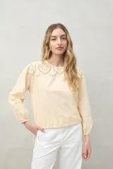 Blusa color verde claro de algodón con cuello a la base y bordados calados en el canesú. Presenta mangas largas con pequeñas aberturas lineales y ajuste con elástico en el puño.