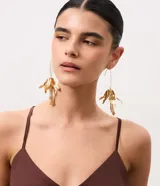 Aros maxi colgantes de metal dorado con diseño de flor de lirio, pétalos alargados y cadenas colgantes con cuentas en el centro.