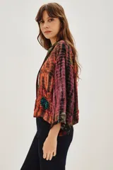 Kimono de estilo abierto con mangas anchas, confeccionado en viscosa con un diseño estampado que combina patrones tipo tie-dye y patchwork en tonos vibrantes. Presenta detalles de aplicaciones decorativas y forro interior.