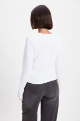 Remera de manga larga con textura acanalada y silueta ajustada. Presenta cuello redondo y un pequeño bordado decorativo en el centro del pecho.