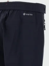 Pantalón técnico de corte recto en color azul marino, con cierre frontal, bolsillos laterales con cremallera y detalle de botón a presión en la cintura.