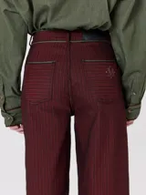 Pantalón sastrero de tiro medio, pierna ancha y corte recto, color bordó con finas rayas verticales y detalles de vivos a contratono en la pretina y el frente.