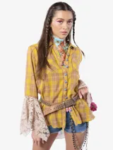 Camisa de algodón a cuadros en tonos amarillos y marrones, con mangas largas que terminan en volantes de encaje beige. Presenta botones metálicos frontales, uno de ellos con detalle de cristal, y un aplique floral bordado en 3D en una de las mangas.