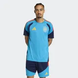 Camiseta de entrenamiento de fútbol Adidas para hombre, color celeste vibrante con textura de micro-puntos. Presenta detalles en azul marino en las mangas y hombros, con franjas en rojo y amarillo en la parte superior de los hombros. Incluye el escudo de la selección española y el logo de Adidas en amarillo.