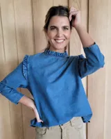 Blusa celeste de denim con cuello alto fruncido y mangas 3/4 con volados en los hombros.