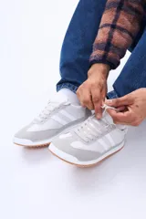 Championes urbanos de diseño retro, combinan paneles de gamuza gris en la puntera y talón con cuerpo de material sintético negro. Presentan dos franjas laterales blancas, cordones negros y suela de goma con base color caramelo.