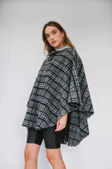 Poncho de paño con estampa a cuadros en tonos grises, negros y blancos, con cuello camisero gris y cierre frontal con dos botones.