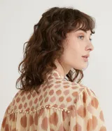 Camisa de gasa color beige con estampado de lunares marrones, cuello mao, mangas 3/4 abullonadas y cierre frontal con botones.