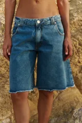 Bermuda de denim azul con corte a la rodilla, diseño de tiro medio y ruedo deshilachado al corte.