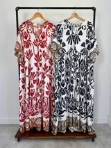 Maxi vestido blanco con estampado paisley en azul marino y detalles en tonos dorados, con cuello en V, mangas amplias y diseño escalonado.