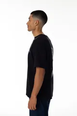 Remera negra de algodón con estampa trasera de un surfista plateado sobre una tabla en el espacio. Logo VERNAL frontal con acabado galáctico.