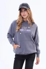 Buzo tipo canguro de felpa color gris, con capucha, bolsillo frontal tipo canguro y estampa frontal con texto y estrellas.