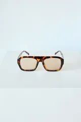 Lentes de sol con armazón de policarbonato en estampado carey y cristales en tono marrón claro. Presentan un diseño de puente plano y forma rectangular.