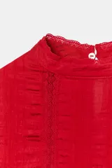 Blusa blanca de cuello alto con detalles de puntilla, manga corta abullonada y cierre posterior con botón.