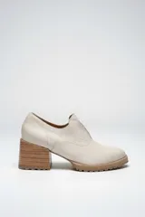 Zapato de cuero color beige, con taco de madera y suela dentada. Presenta un diseño slip-on con detalles de textura en relieve en los laterales y el empeine.
