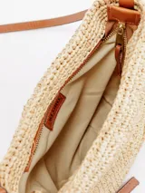 Bandolera de rafia natural de forma redondeada, con correa larga fina de cuero marrón, cierre superior y detalle de aplique en cuero con la letra K.