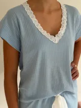 Pijama celeste de algodón acanalado compuesto por una remera de manga corta con escote en V adornado con puntilla blanca, y un short a juego con elástico y lazo de ajuste en la cintura.
