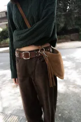 Bolso tipo bandolera de gamuza color marrón, con diseño de medialuna, detalles trenzados en los bordes y flecos decorativos. Cuenta con correa ajustable y desmontable.