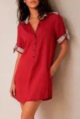 Vestido corto de lino color beige, de corte recto y holgado, con cuello polo y cierre frontal parcial con botones. Las mangas cortas cuentan con detalles de tiras para anudar en los puños.