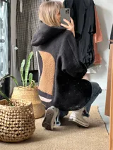 Campera tipo hoodie de textura tipo corderito en color negro, con diseño de collage abstracto en la espalda compuesto por formas geométricas en tonos marrón y rosado. Presenta capucha, mangas largas y un corte holgado.