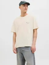 Remera color crema de algodón con cuello redondo y mangas cortas. Estampa en el frente con un paisaje costero, un auto rojo y la inscripción "Casares Málaga The creative studio".