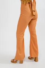Pantalón de tiro alto con corte flare, confeccionado en lino color naranja. Presenta costuras verticales frontales que estilizan la silueta.