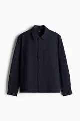 Sobrecamisa de tejido suave color azul marino, con cuello inglés, tapeta lisa y botones frontales. Presenta dos bolsillos superiores abiertos y canesú en la espalda.