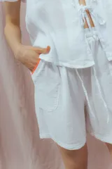 Short blanco de calce relajado con cintura elástica y lazo regulable. Presenta bolsillos amplios con ribete interior de color naranja neón.