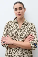 Vestido camisero midi con estampado geométrico en tonos verde oliva y beige. Presenta cuello camisero, cierre frontal con botones, mangas tres cuartos y aberturas laterales en el ruedo.