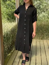 Vestido camisero largo negro, confeccionado en lino, con cuello, botones frontales de nácar y aberturas laterales en el bajo.