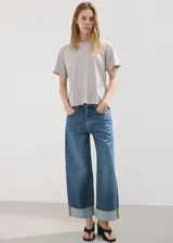 Jeans estilo wide leg de tiro medio con diseño de cinco bolsillos, trabillas para cinturón, cierre de botón y cremallera, y bajo vuelto.