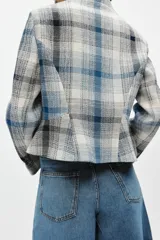 Blazer de corte peplum con cuello redondo y manga larga. Confeccionado en tejido de textura con mezcla de algodón y lino, presenta un estampado de cuadros en tonos azules y blancos. Incluye forro interior y cierre frontal mediante ganchos metálicos.