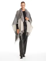 Ruana tejida con diseño color block en tonos grises y beige, con cuello de piel sintética y terminación en flecos.