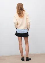 Jersey de punto grueso en color crema con cuello en V y detalles en contraste oscuro en el cuello y puños. Presenta un diseño recto de manga larga con una camisa de cuello camisero integrada en color celeste.